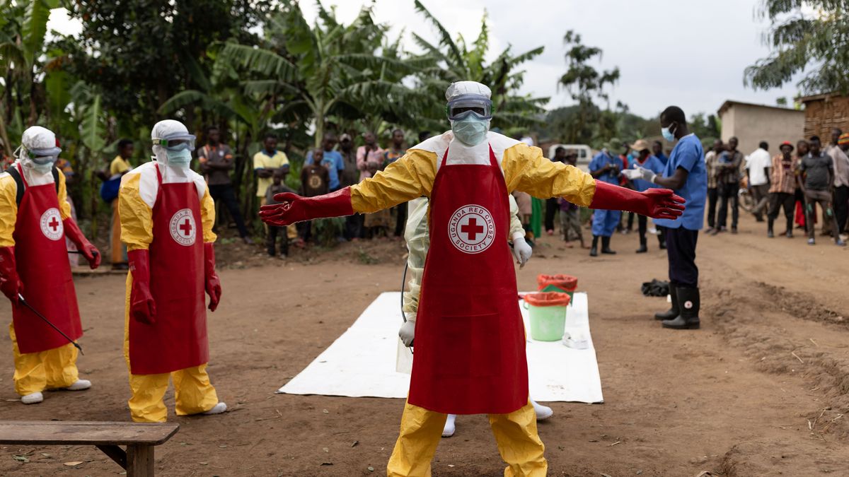 A Ugandan Red Cross worker in protective gear stands with outstretched arms at a burial site on Oct. 11, 2022.